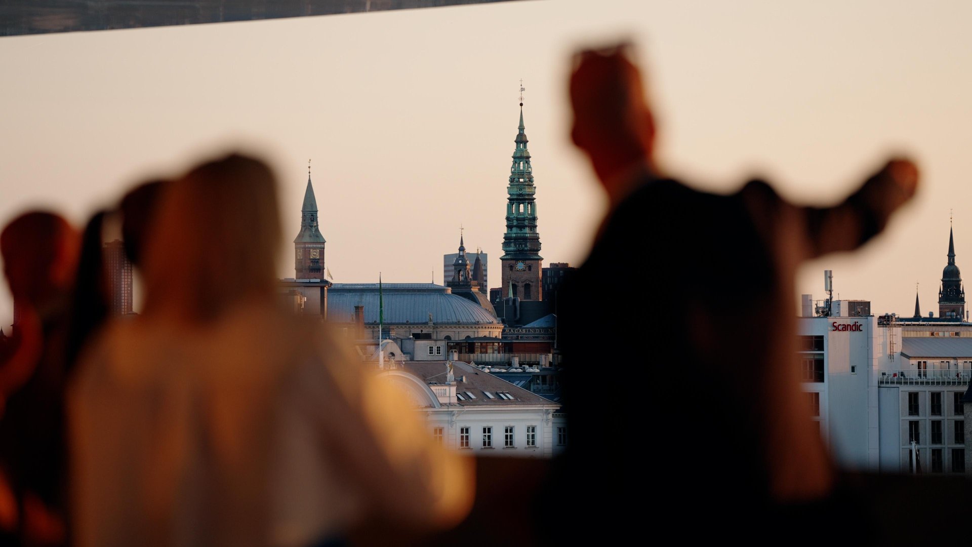 Guests looking across Copenhagen rooftops and spires in warm evening light.
